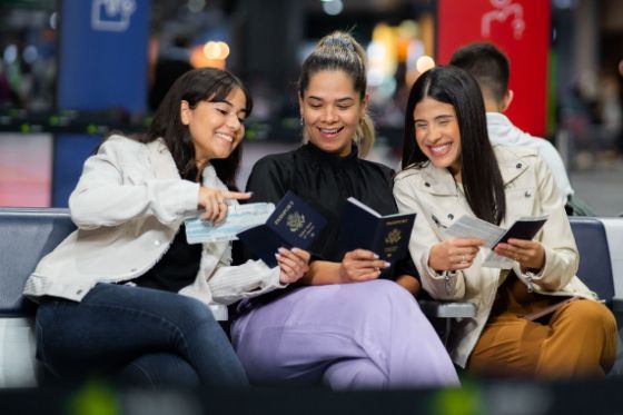 3 women sitting at an airport looking at their passports