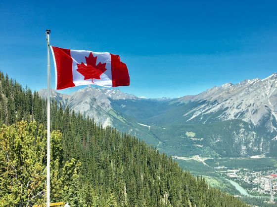 A Canadian flag flying in front of a forested mountain and blue sky view