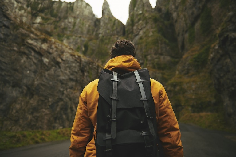 man wearing a backpack facing mountains.