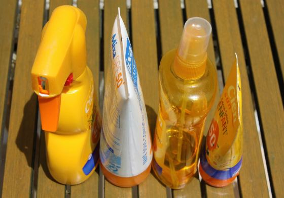 several bottles and tubes of sunscreen on a wooden deck