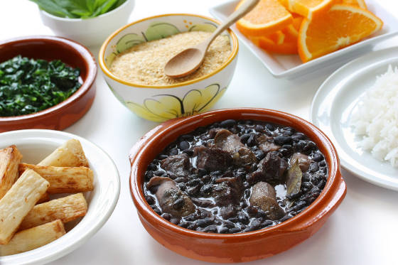 Brazilian food including feijoada, farinha de mandioca, fried macaxeira and white rice.