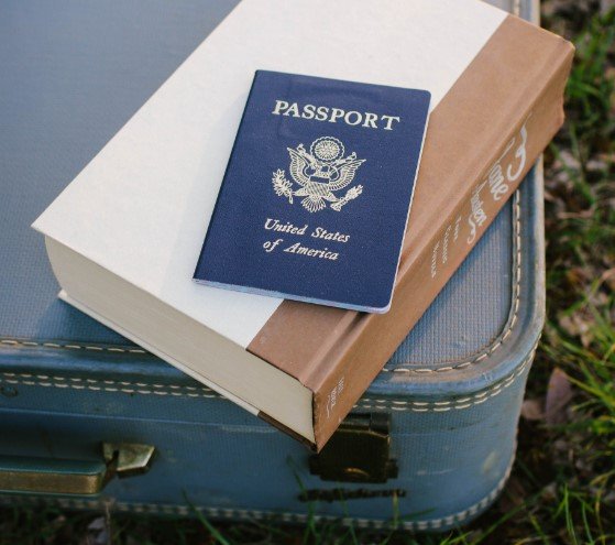 passport laying on a book and suitcase in the grass