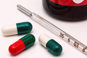 three pills and a thermometer on a white surface