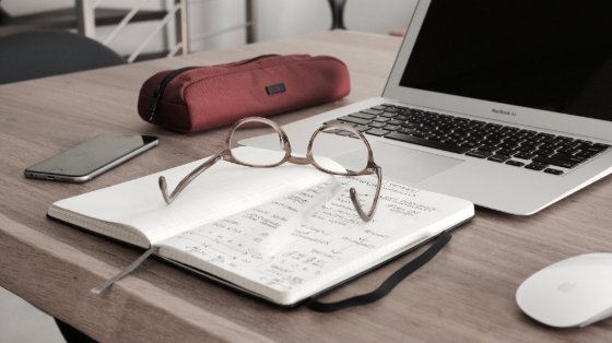 glasses resting on a notebook in front of a laptop