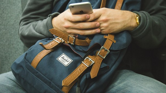 man sitting with bag in lap using phone